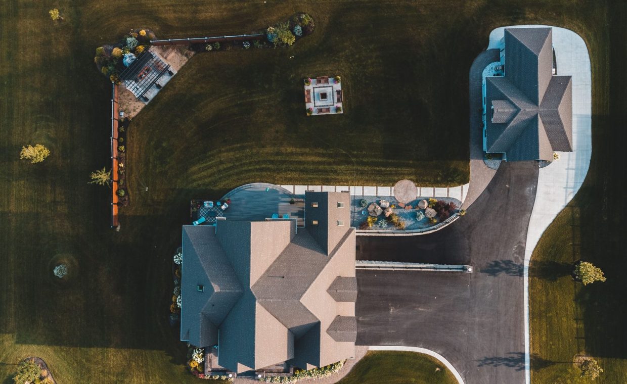 Drone view of suburban neighborhood with houses, driveways, and landscaped gardens.