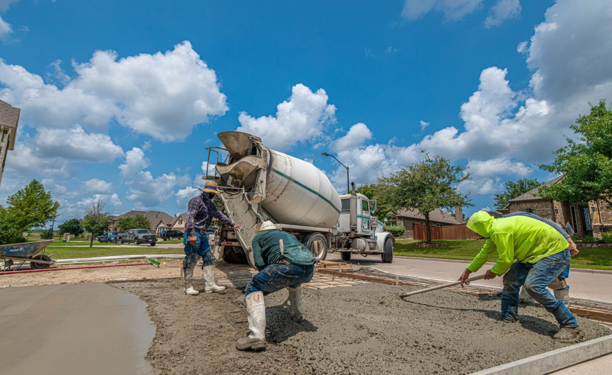 Construction workers laying concrete for a driveway in Fort Worth, Texas, under a bright blue sky.