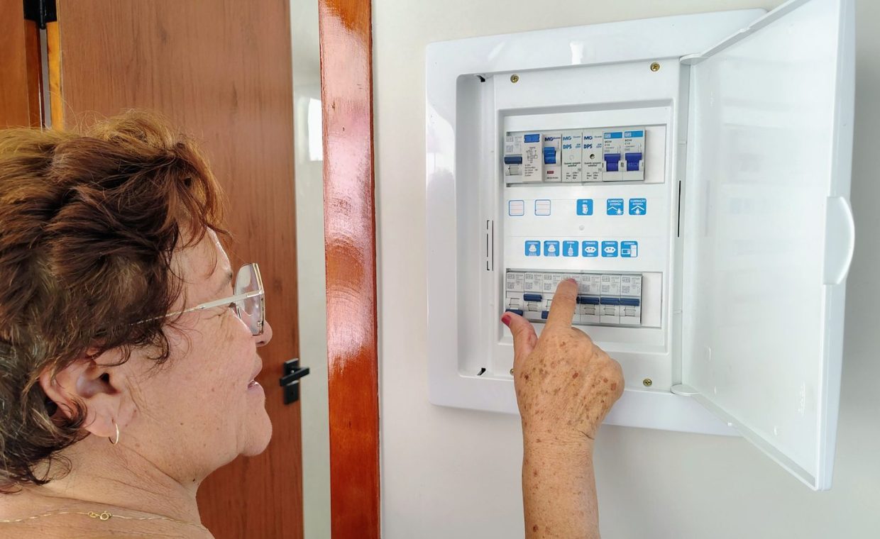 A senior woman is adjusting an electrical fuse panel indoors, demonstrating home safety.