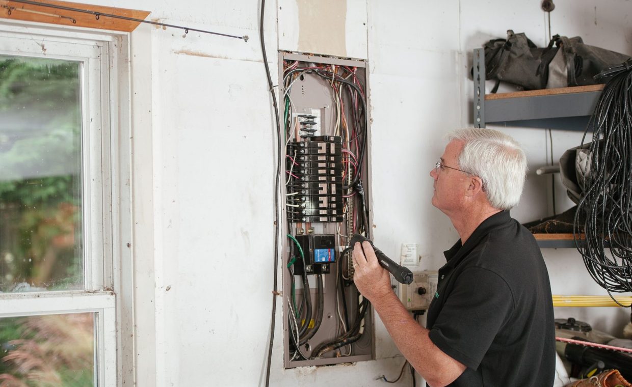An electrician carefully examines a residential fuse box indoors, ensuring electrical safety and compliance.