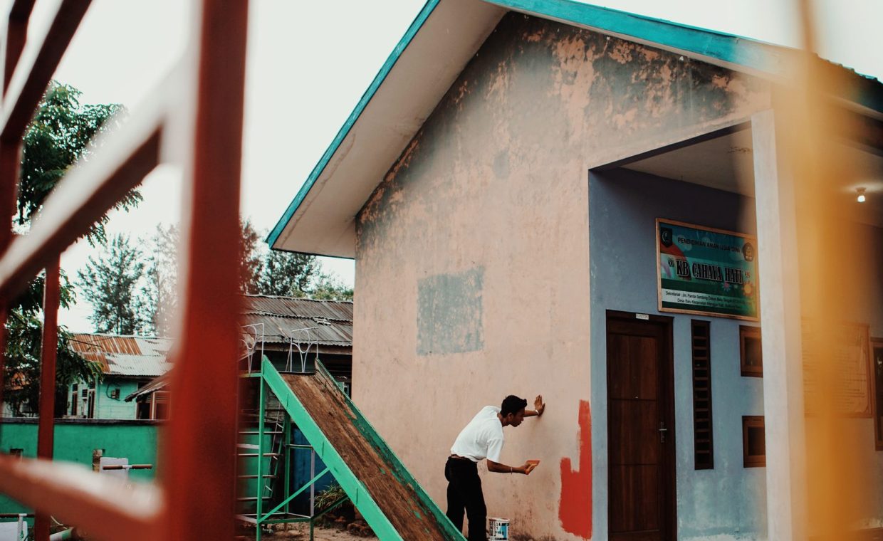 A person painting a building's exterior wall outdoors during the day.