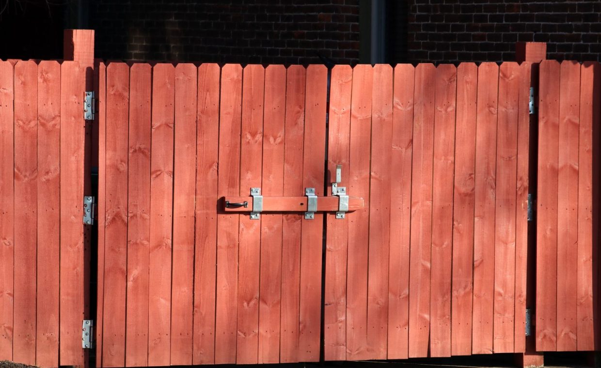Rustic red wooden fence with a metal latch, ensuring safety and security outdoors.
