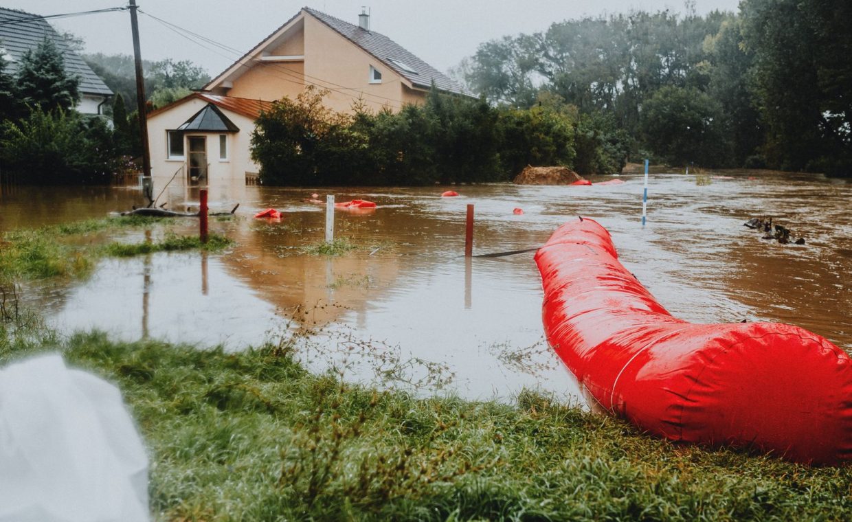 Flooded residential area protected by red flood barriers, showing severe weather impact.