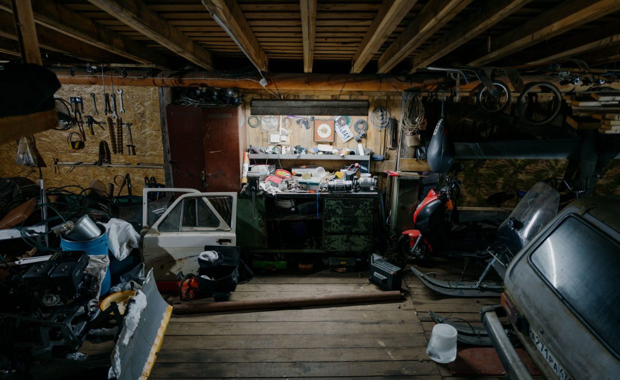 A cluttered garage workshop filled with vintage tools, car parts, and motorcycles, showcasing a rustic work environment.