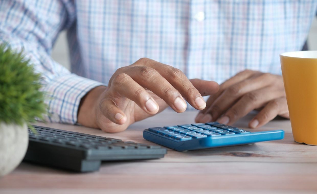 person using calculator at desk with coffee mug