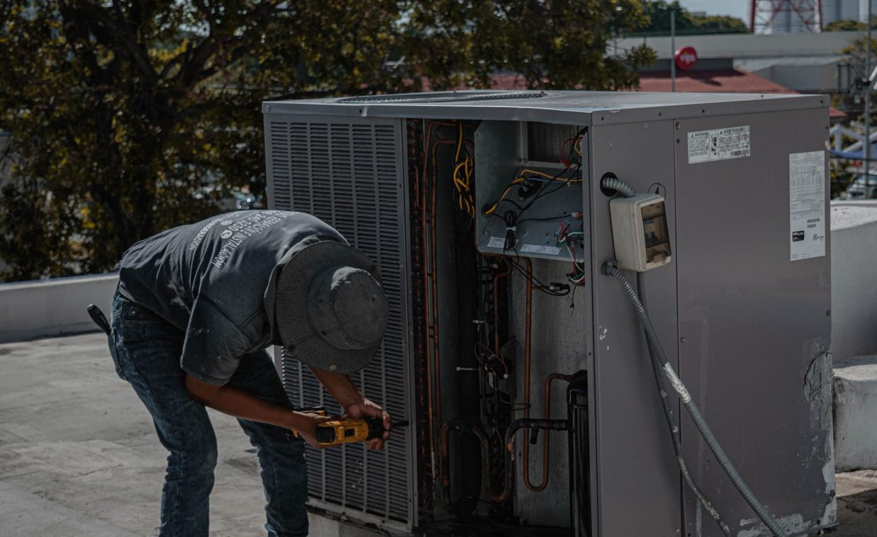 A technician is repairing an air conditioning unit on a rooftop, demonstrating skilled manual work.