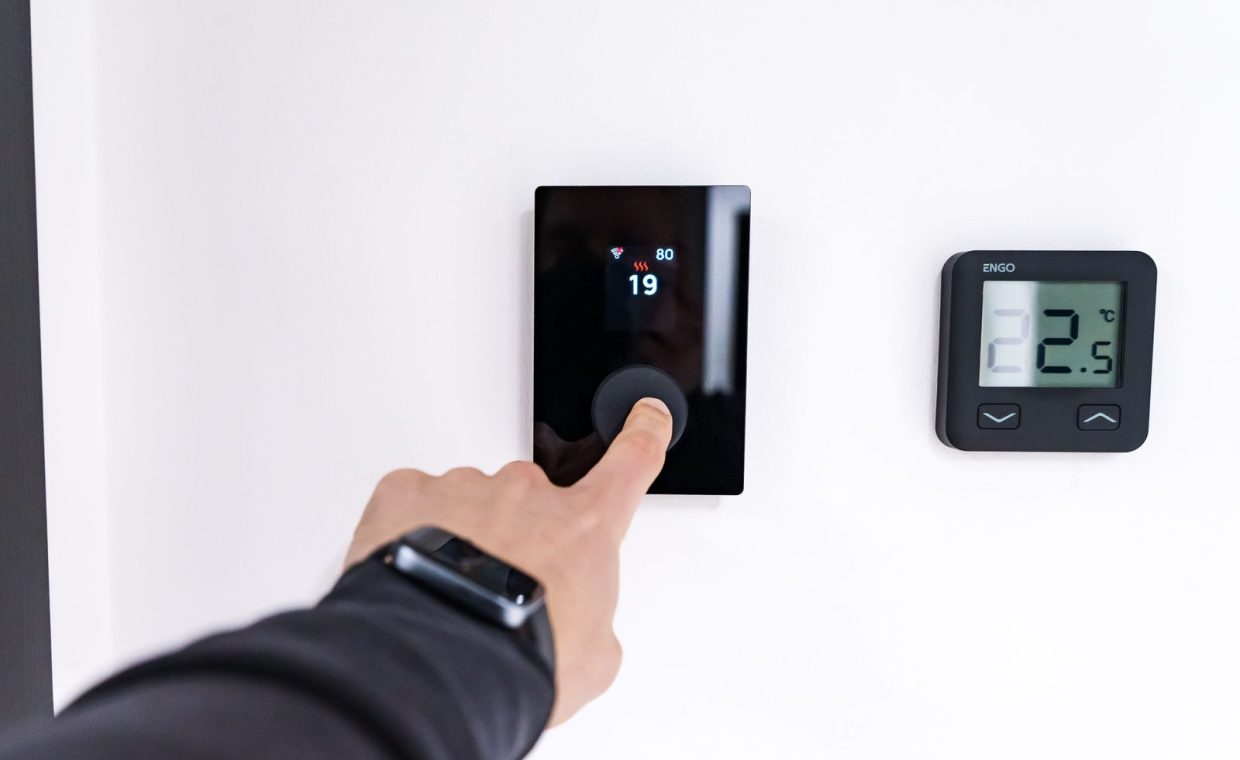 A hand adjusting a digital thermostat in a modern home interior, showcasing smart home technology.