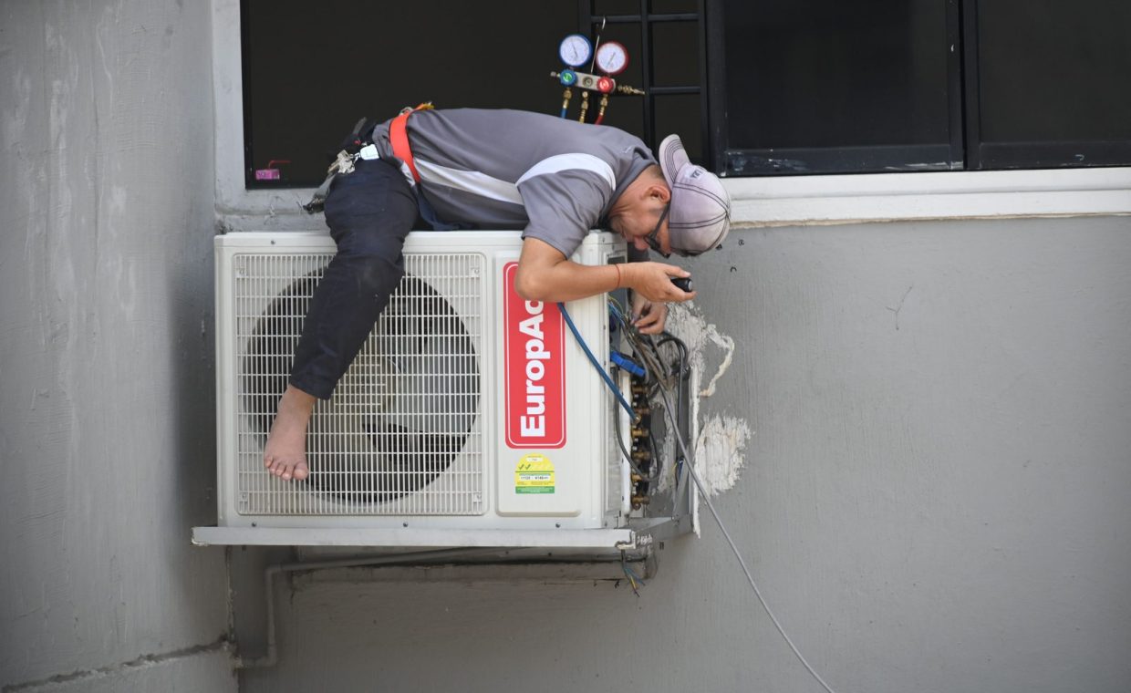 A technician skillfully repairing an outdoor air conditioning unit mounted on a building wall.