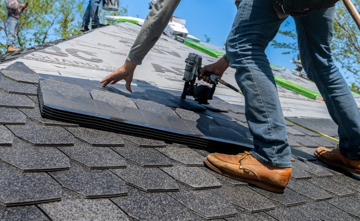 Roofer using nail gun for shingle installation on residential roof.