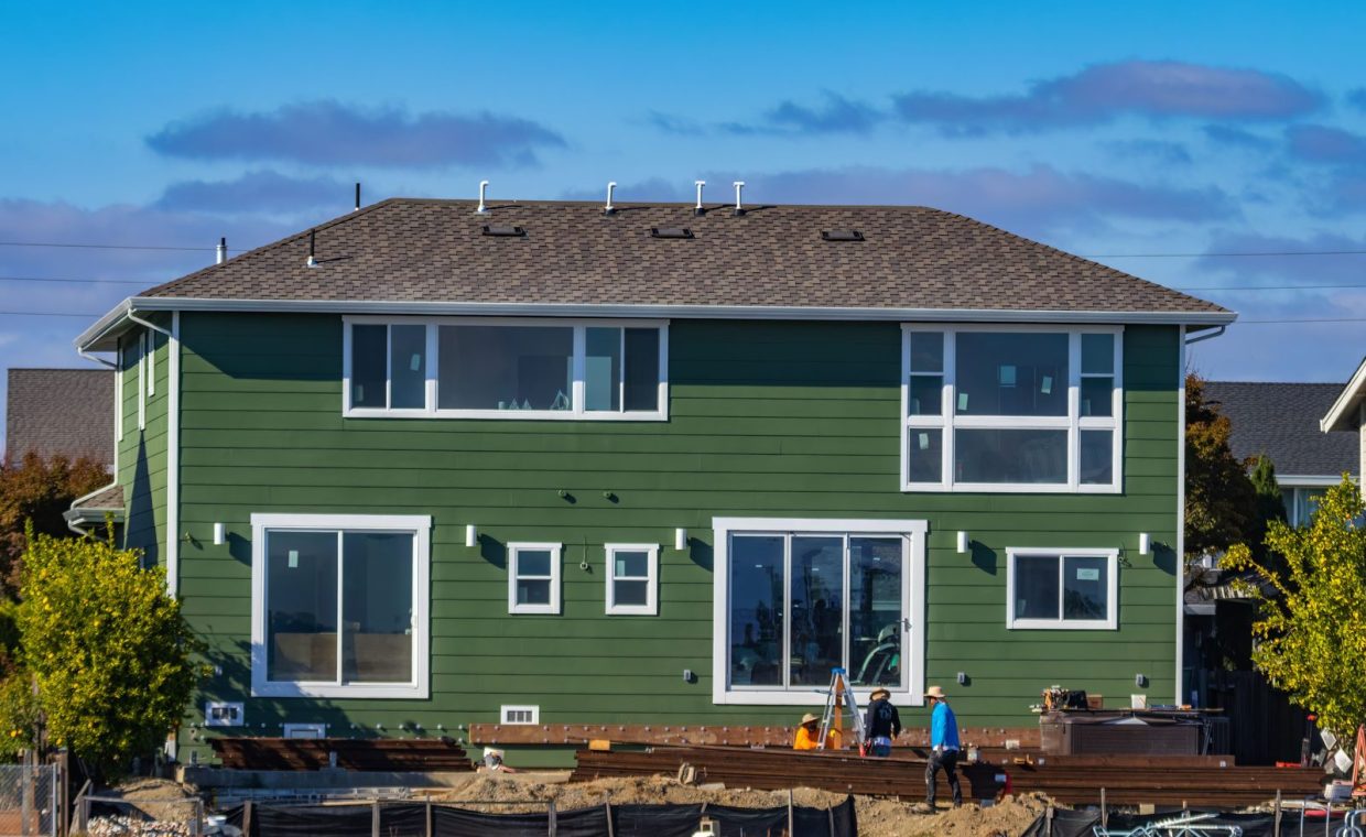 A modern green house under construction with blue skies and workers outside.