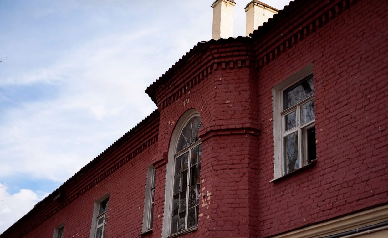 A detailed view of a red brick building facade with an arched window under a blue sky.