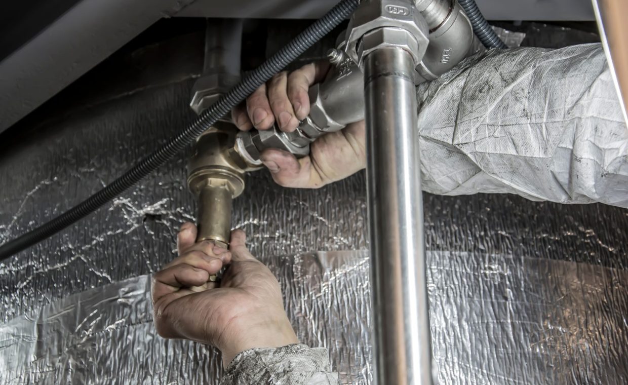 Close-up of a plumber's hands installing steel pipes indoors, showcasing skilled manual work.